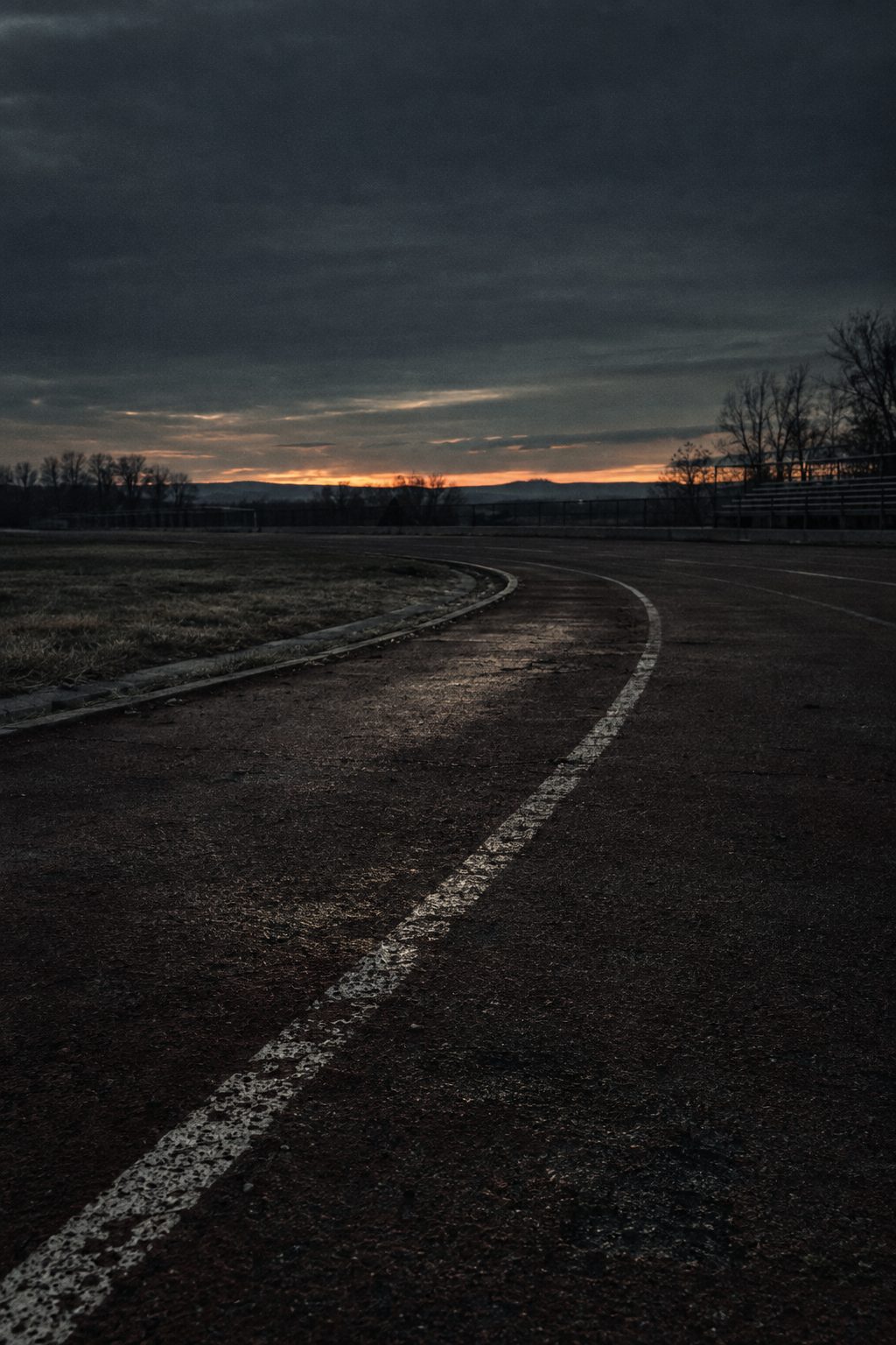An empty running track curving away at dusk under heavy cloud.