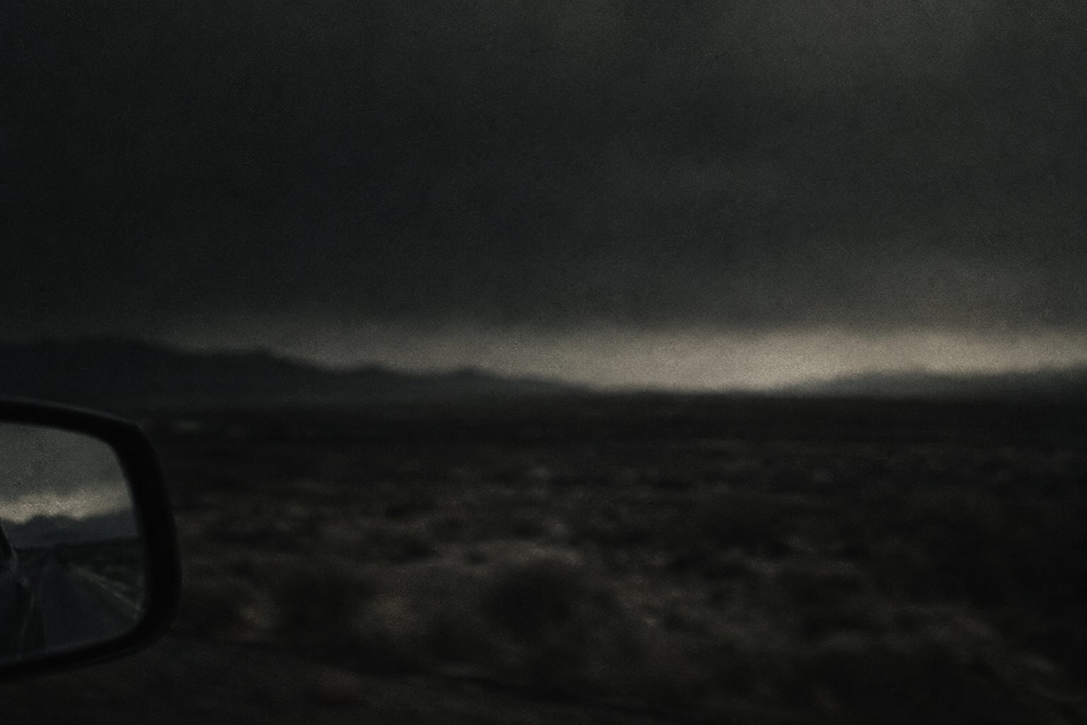 A dark side mirror at the edge of the frame, a blurred landscape beyond.